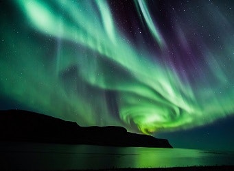 A swirl of green and purple northern lights over landscapes in Iceland